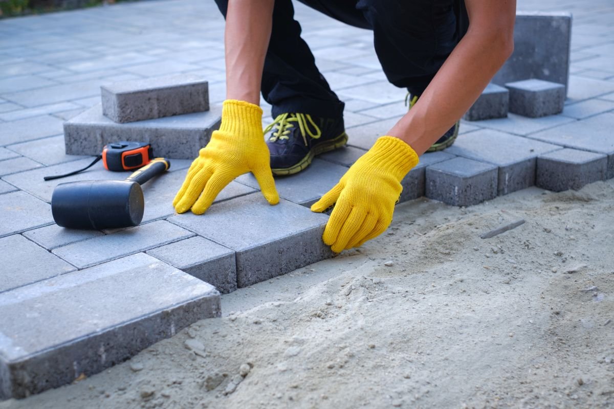 The master in yellow gloves lays paving stones